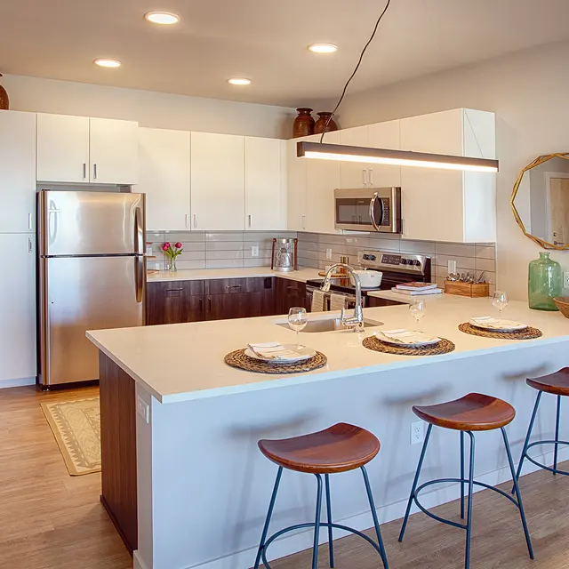 Modern kitchen with stainless steel appliances, white cabinetry, and a large island featuring bar stools and decorative accents.