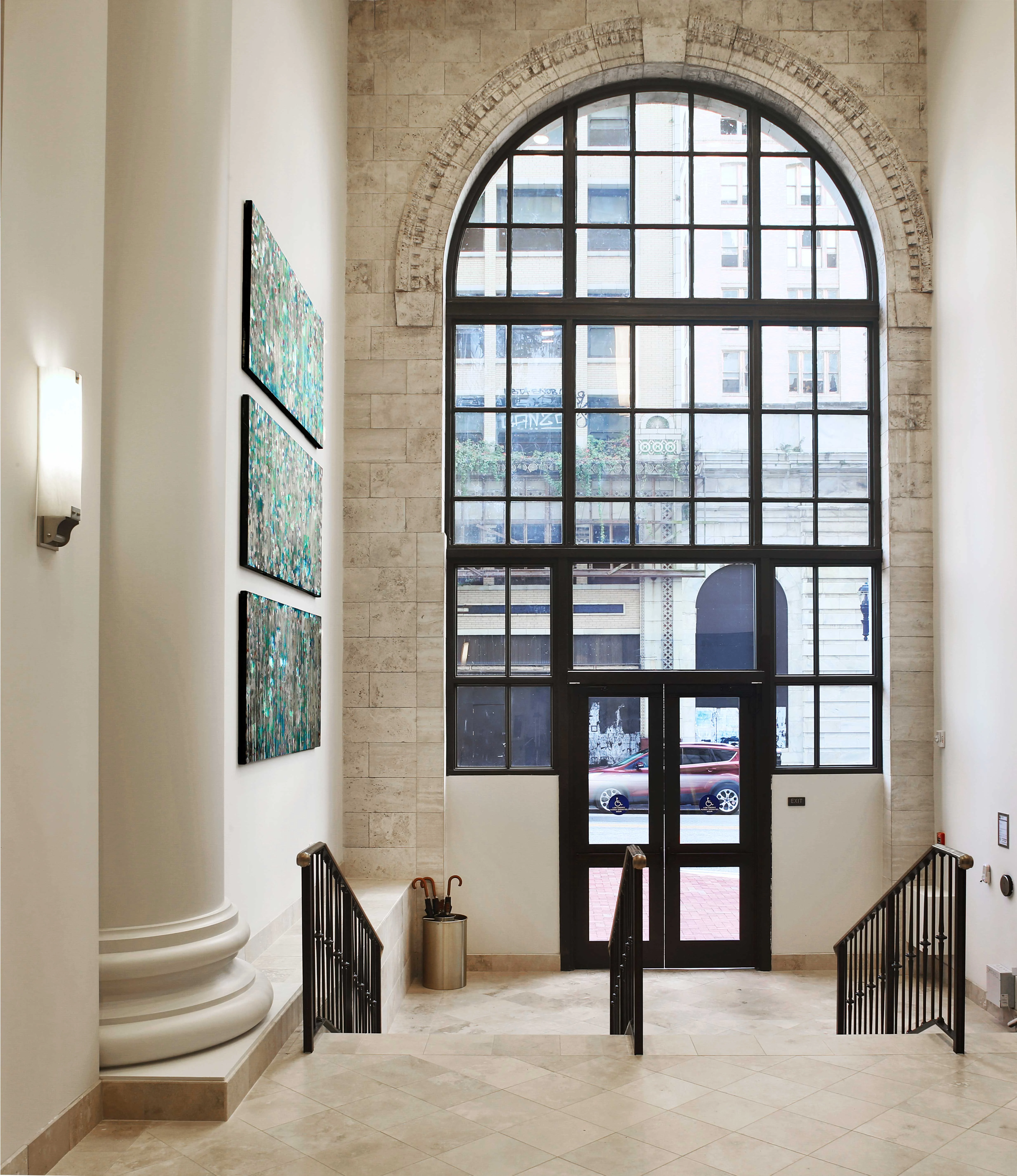 Stairway with Arched Window An interior view of a stairway leading to a large arched window, with modern artworks on the wall and a glimpse of the street outside.