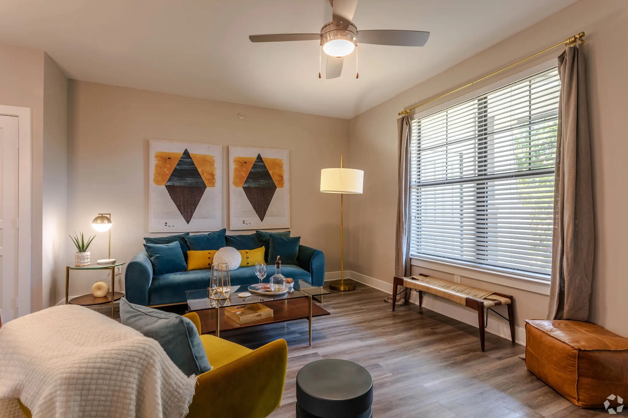 Furnished living room with two large windows for natural lighting, ceiling fan with lighting on hardwood-style flooring.