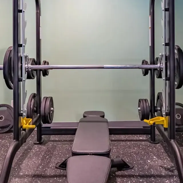 Weight lifting equipment including a barbell with weights and a padded bench in a gym setting.