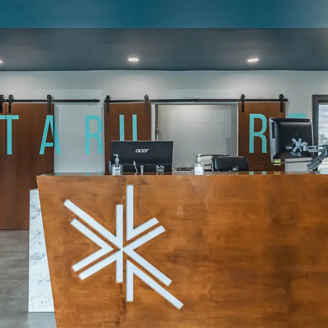 A modern reception area featuring a wooden front desk with a marble accent, large sliding doors with the letters 'STAR' above, and a sleek, contemporary design.