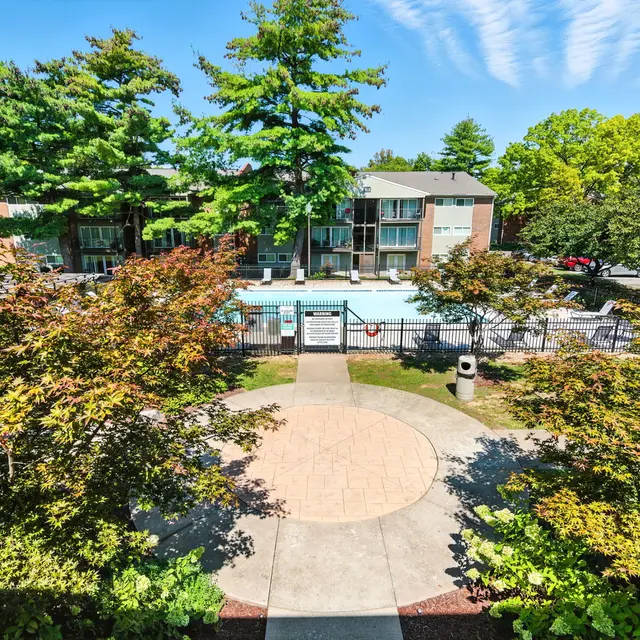 View of a pool area surrounded by lush greenery and apartment buildings under a clear sky.