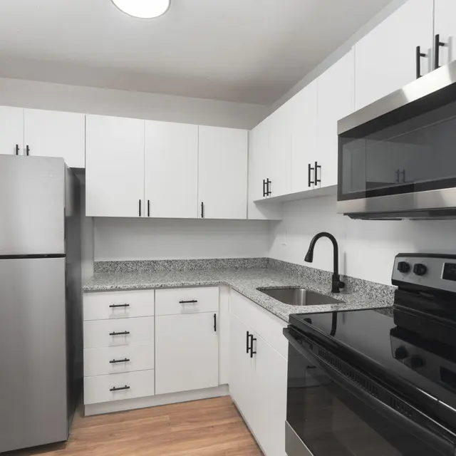 A modern kitchen featuring a stainless steel fridge, black stove, and gray countertops under white cabinets.