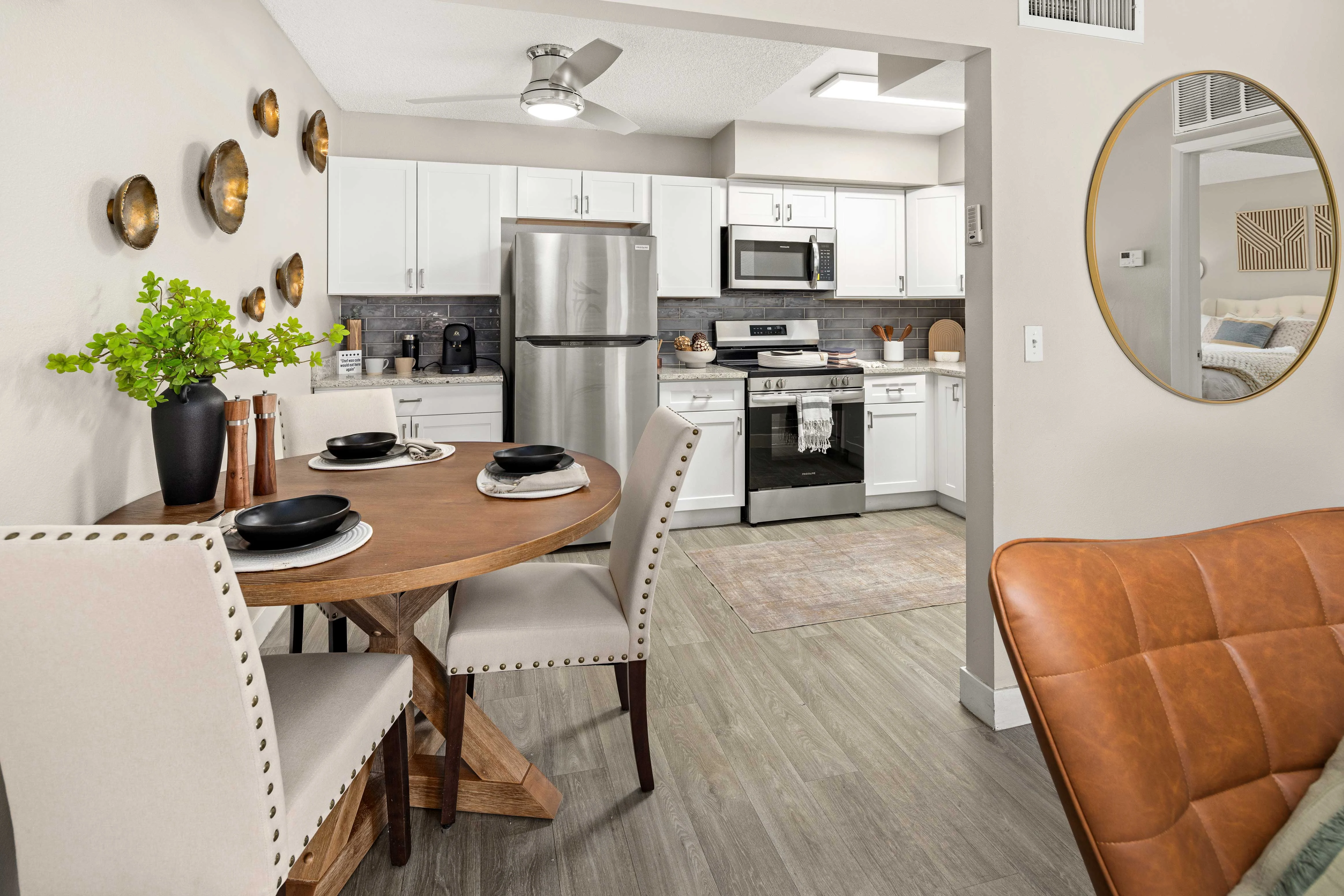 Modern Kitchen and Dining Space A modern kitchen and dining area featuring a round wooden table with four chairs, a stainless steel refrigerator, and white cabinetry. Decorative wall plates are displayed, and a potted plant adds a touch of greenery.