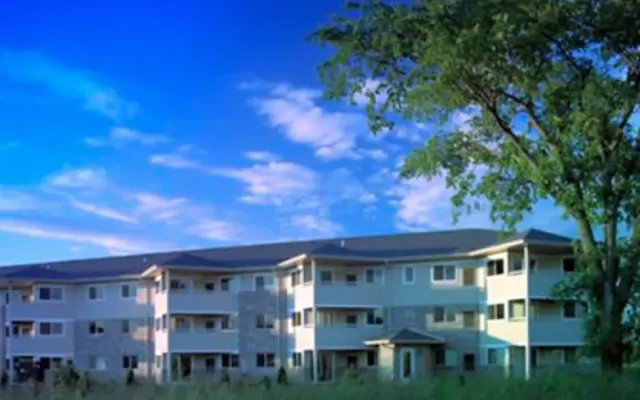 A modern multi-story residential building with balconies under a blue sky with wispy clouds.