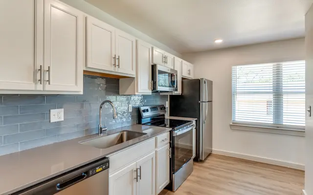 Modern Kitchen Design A modern kitchen featuring stainless steel appliances, white cabinetry, and a light gray backsplash with ample natural light from a window.