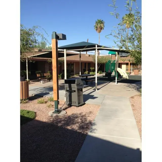 Outdoor Play Area with Playground An outdoor play area with a playground structure, shaded seating, and palm trees under a clear blue sky.