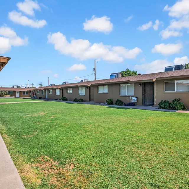 View of an apartment complex with green lawn and blue sky.
