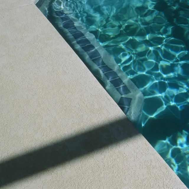 A close-up view of a swimming pool corner showing the water and surrounding deck.