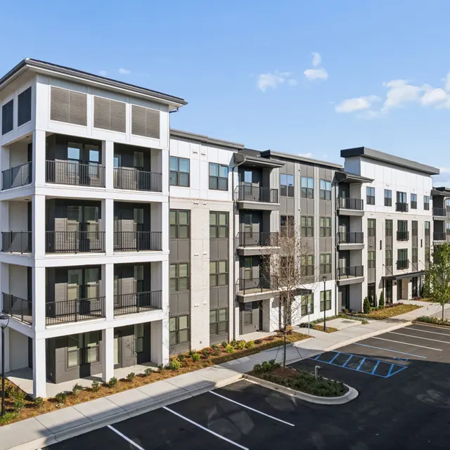 Modern Apartment Building Exterior A modern apartment building with multiple stories, featuring balconies and a landscaped area, set against a blue sky.