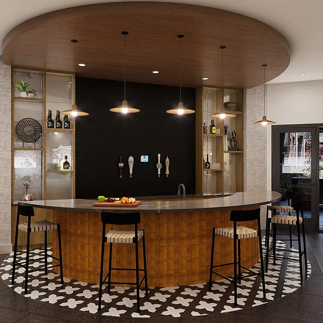 A contemporary bar area featuring a curved wooden counter, high chairs, and a patterned floor with decorative tiles. The back wall showcases shelves with bottles and accessories, illuminated by pendant lights. Large windows are visible, providing natural light.