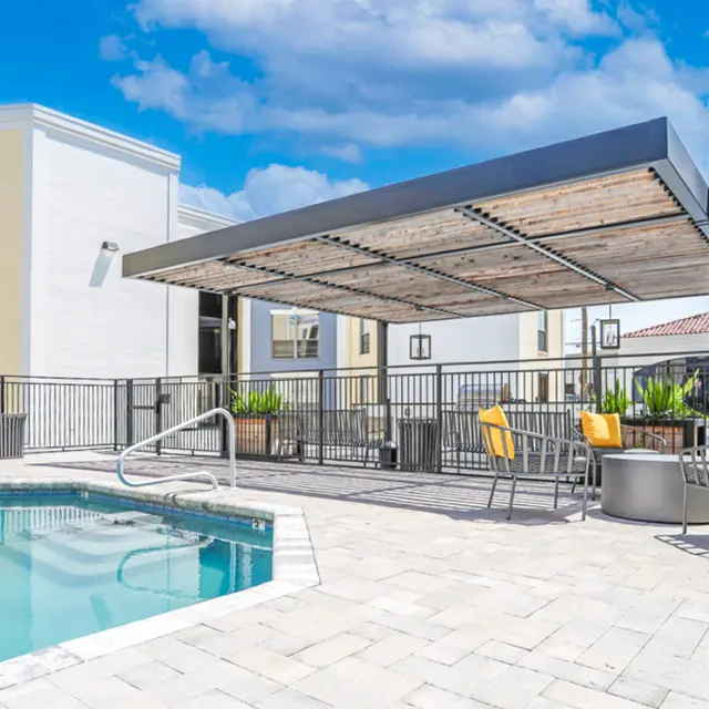 A modern pool area featuring a swimming pool, lounge chairs, and a shaded seating area with tables and chairs.