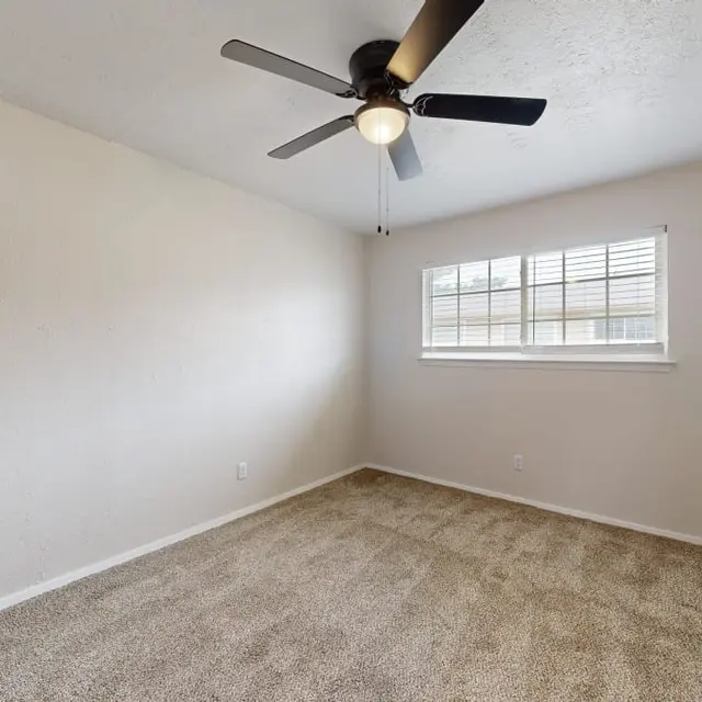 An empty bedroom featuring a ceiling fan, light-colored walls, and a window with blinds.