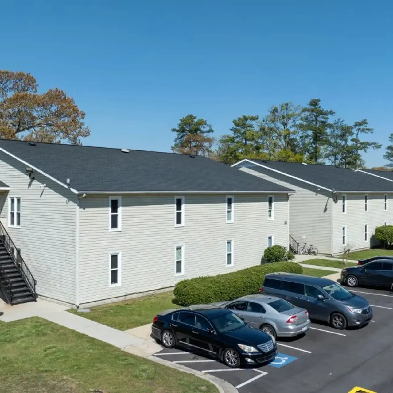 Aerial view of a two-story apartment complex surrounded by green grass and parked cars.