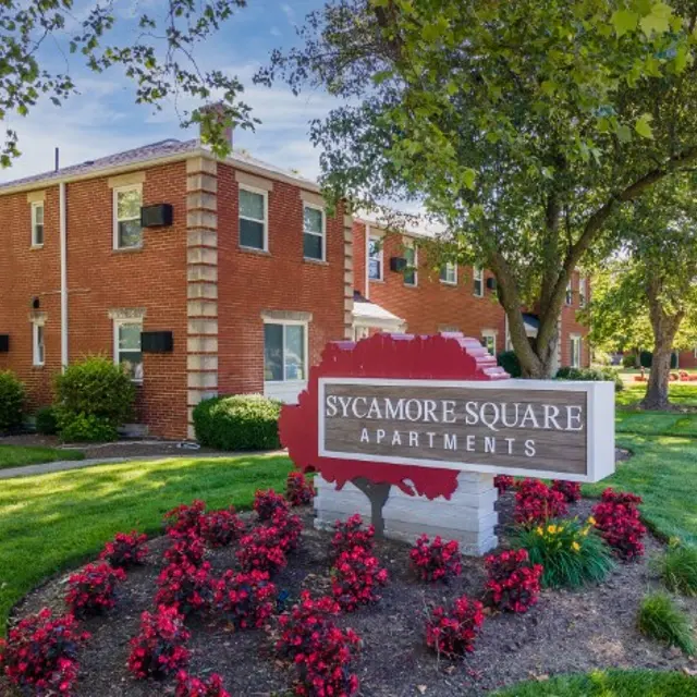 Exterior view of Sycamore Square Apartments with red brick buildings and flower beds.