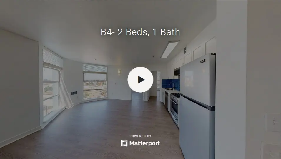 Interior view of a two-bedroom, one-bath apartment showcasing a bright, spacious layout with large windows and modern kitchen appliances.