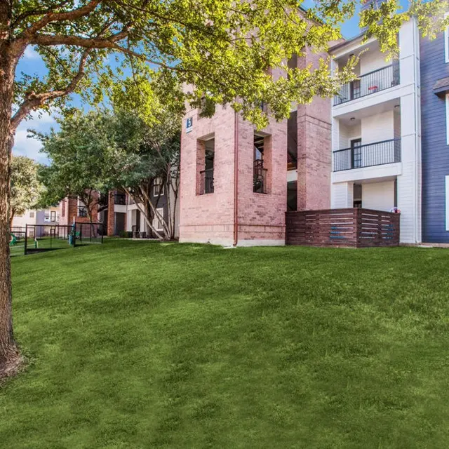 View of an apartment complex exterior with green grass and trees.