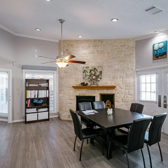 Modern Dining and Living Area Interior of a modern dining and living area featuring a stone fireplace, dining table with black chairs, and large windows.