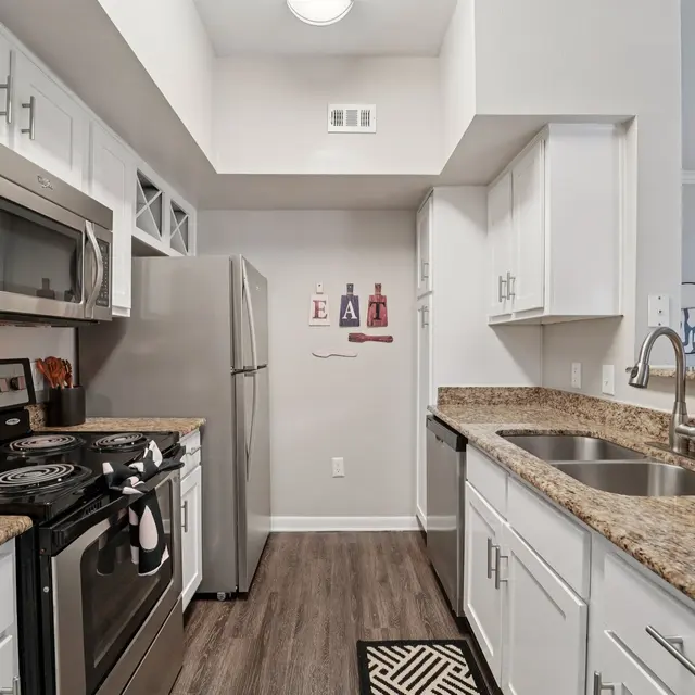 A modern kitchen featuring stainless steel appliances, granite countertops, white cabinets, and a contemporary design. It includes a stove, microwave, refrigerator, and a double sink.