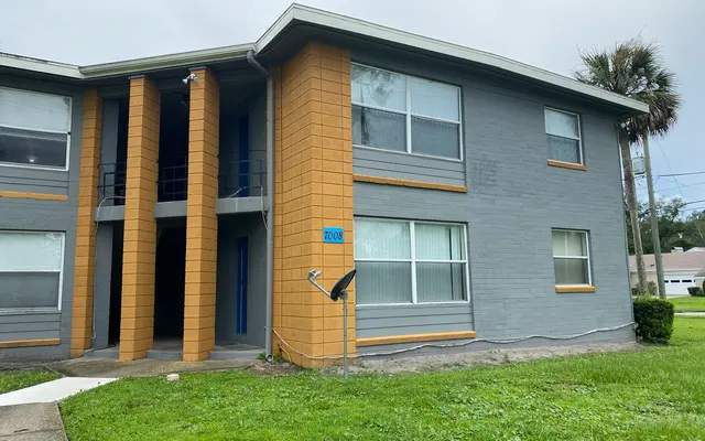 Exterior view of a two-story apartment building with orange and gray walls, large windows, and a green lawn in front.