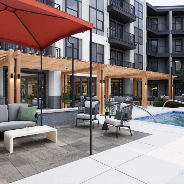 A modern pool area with a seating arrangement under a red umbrella, surrounded by apartment buildings.