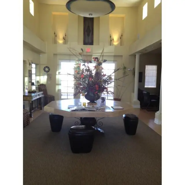 Spacious Lobby Interior A spacious lobby with high ceilings featuring a large decorative flower arrangement on a central table. The flooring is carpeted with dark accent chairs and large windows providing light.