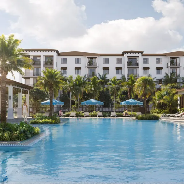A scenic view of a luxury resort pool area surrounded by palm trees and lounge chairs on a sunny day.