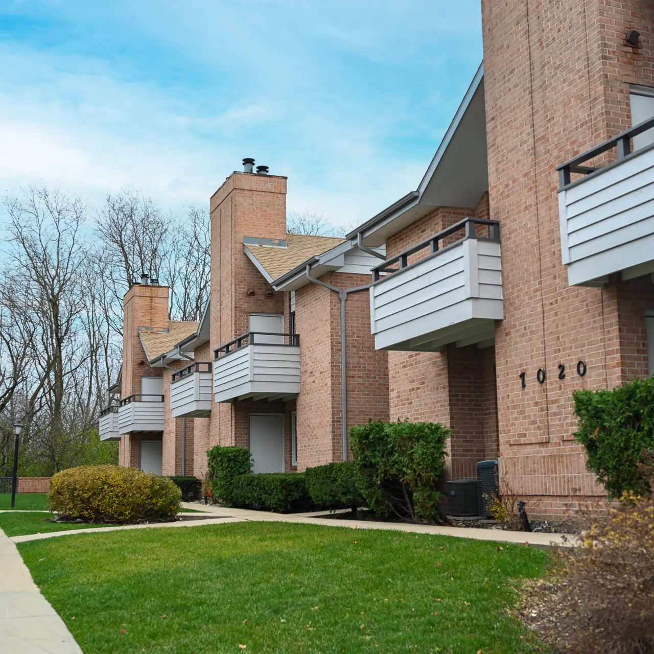Exterior view of a multi-unit apartment building with a sidewalk and landscaped lawn.