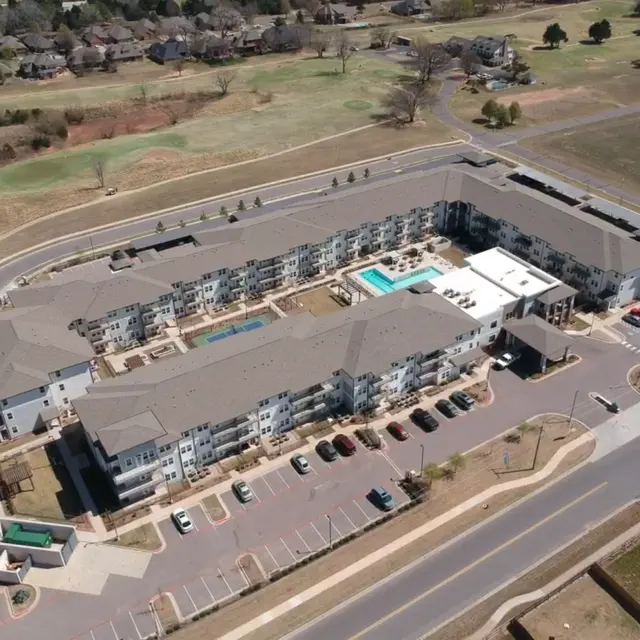 Aerial View of Sage at Cobblestone Creek Aerial view of a modern apartment complex featuring a swimming pool and parking area.