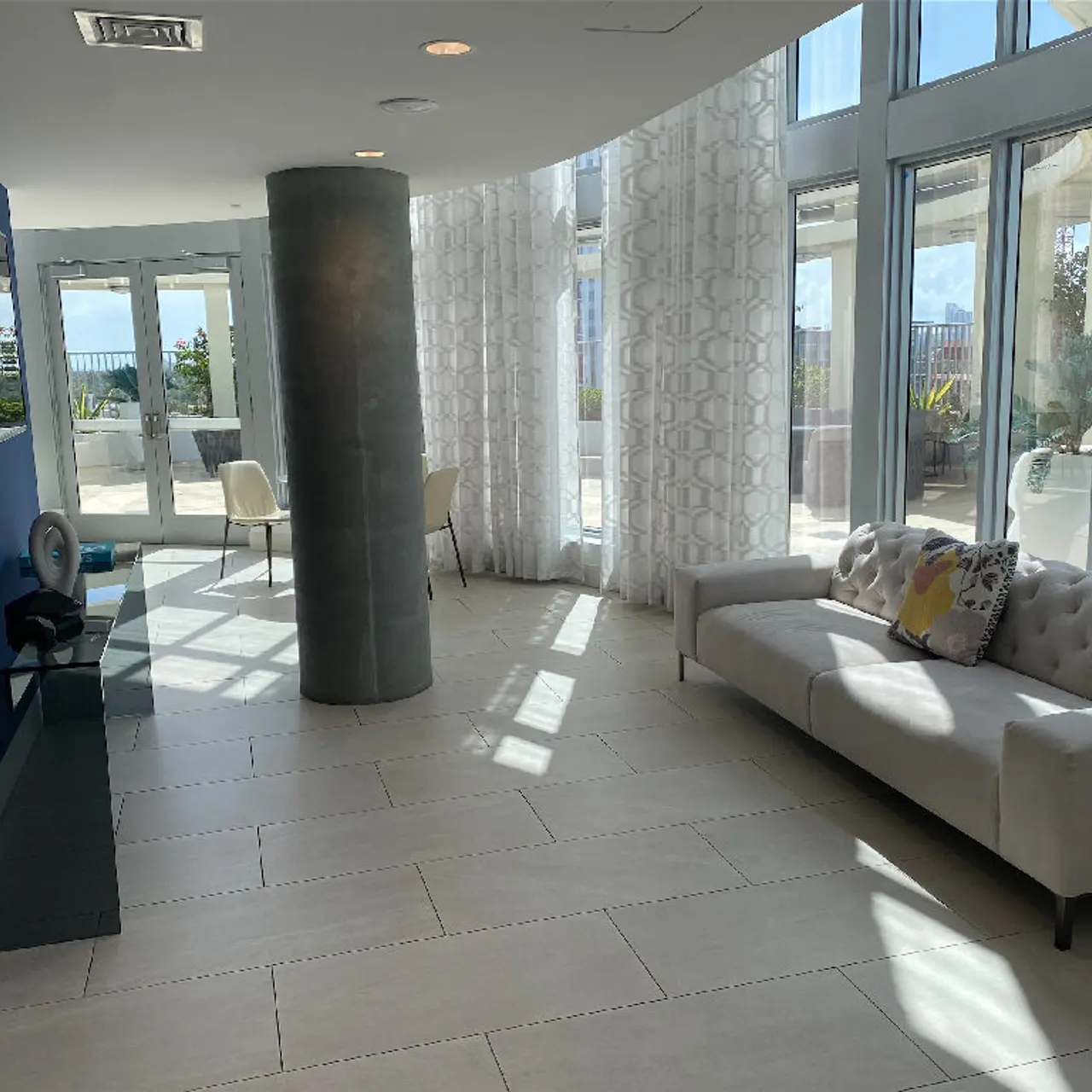 Bright, modern living area with large windows and plenty of natural light. Features a couch with decorative pillows, a blue accent wall, and a tall column.
