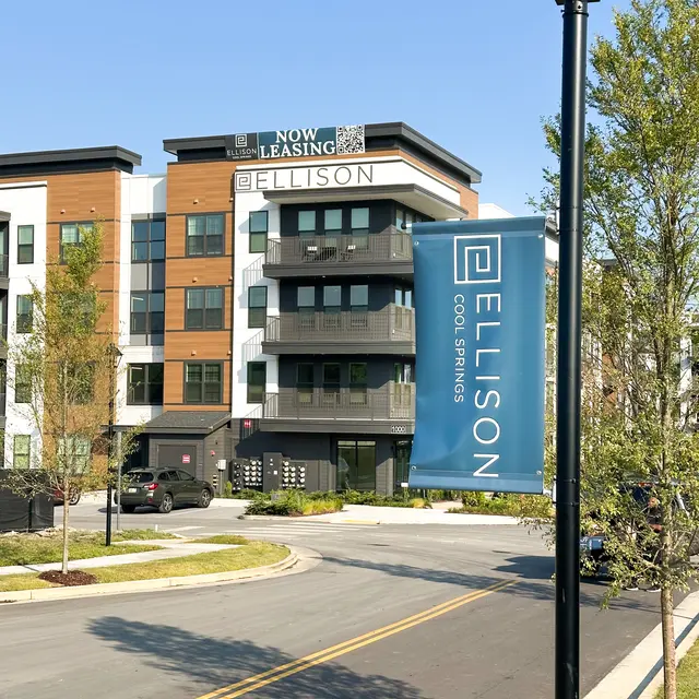 Ellison Apartments in Cool Springs A modern apartment building with a leasing banner, surrounded by trees and a clean road.