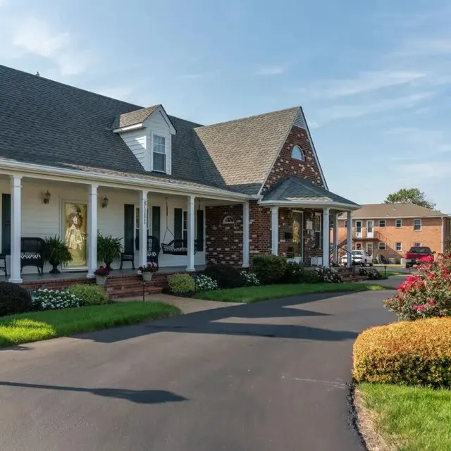 A charming house with a well-maintained lawn and flower beds, featuring a porch with seating and a brick accent wall.