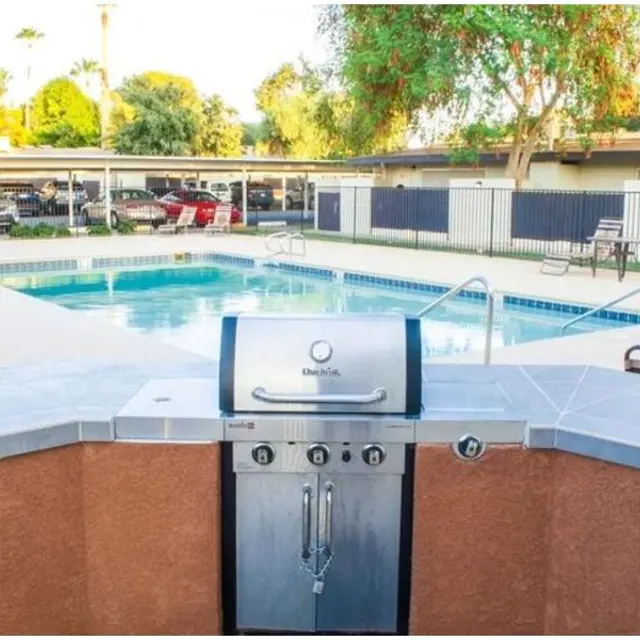 Poolside BBQ Area A well-maintained outdoor area featuring a BBQ grill in the foreground and a clear swimming pool in the background surrounded by lounge chairs and greenery.