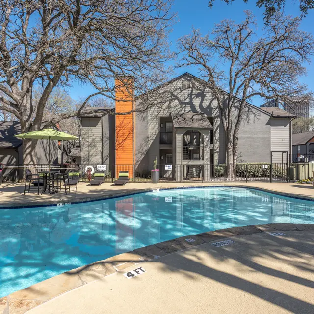 A swimming pool area surrounded by trees and apartment buildings on a clear day.