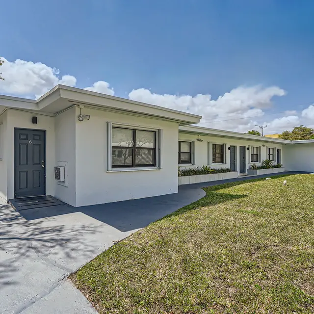 Exterior view of a modern white house featuring a flat roof, large windows, and a front lawn with grass.