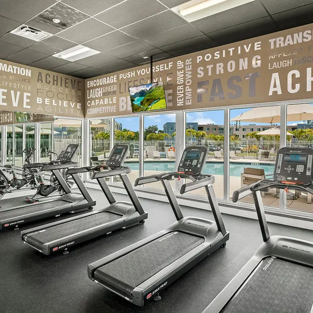 Pine Groves Fitness Center featuring cardio equipment facing tall windows looking towards the community pool. 