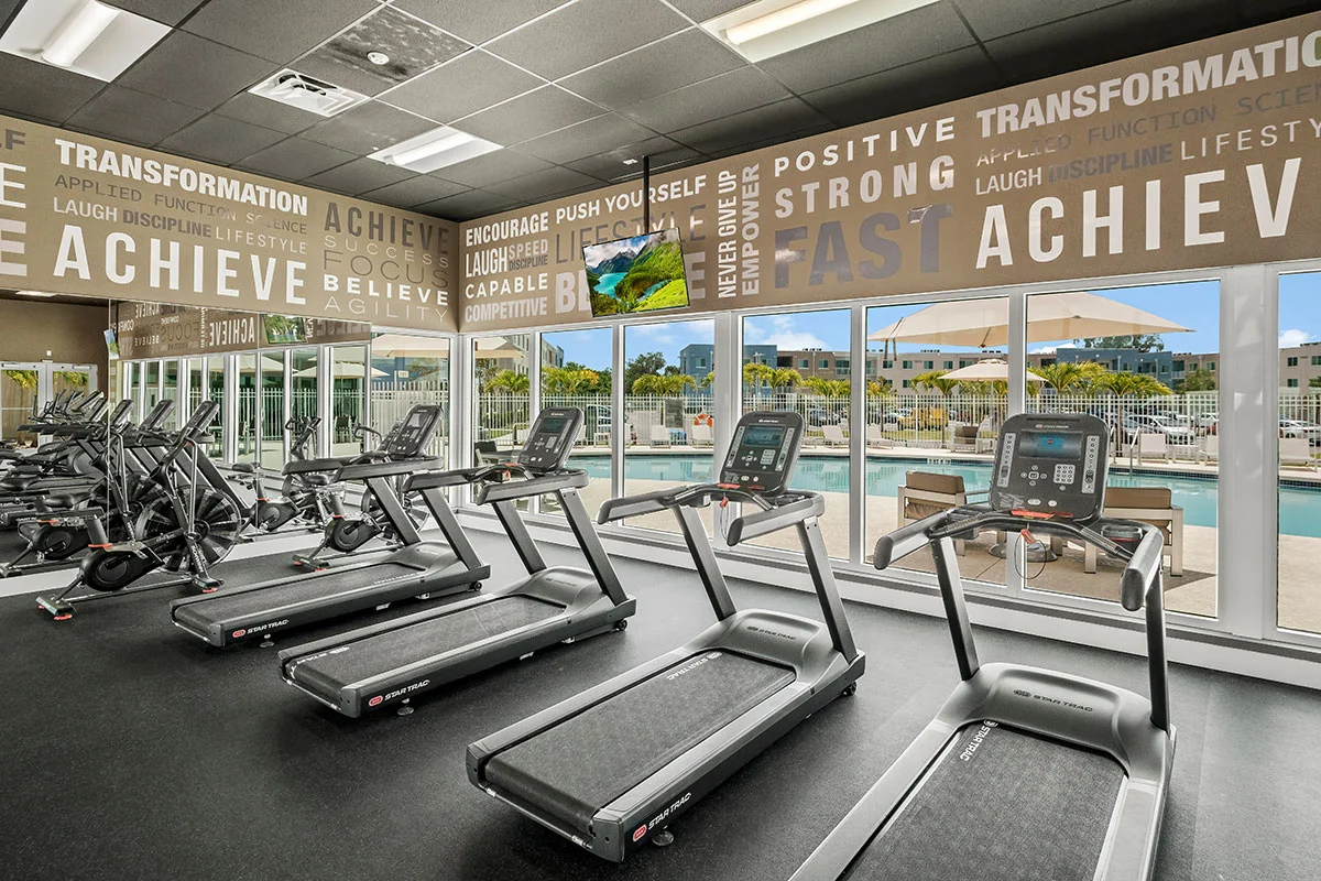 Pine Groves Fitness Center featuring cardio equipment facing tall windows looking towards the community pool. 