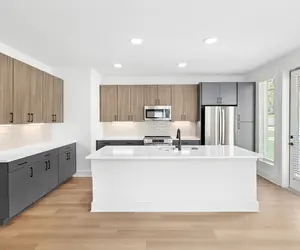 A modern kitchen featuring dark gray and light wood cabinets, stainless steel appliances, and a large white island with a sink.