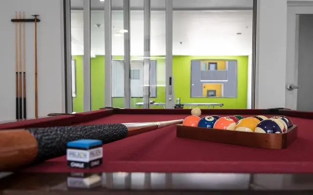 Modern Pool Table Lounge A pool table in a lounge area with colorful balls in a rack and cue sticks in the background.