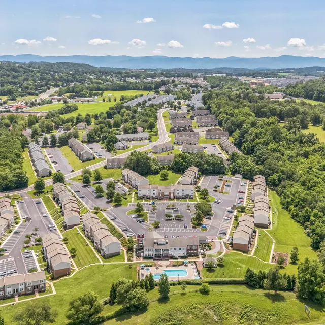 Aerial View of Apartment Complex Aerial view of a spacious apartment complex surrounded by green fields and hills in the background on a sunny day.