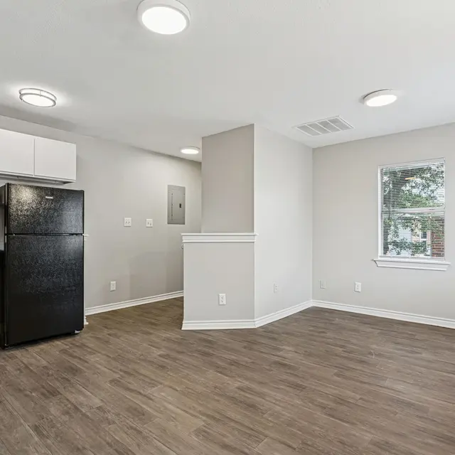 An empty modern kitchen and living area with hardwood floors and a window overlooking greenery.