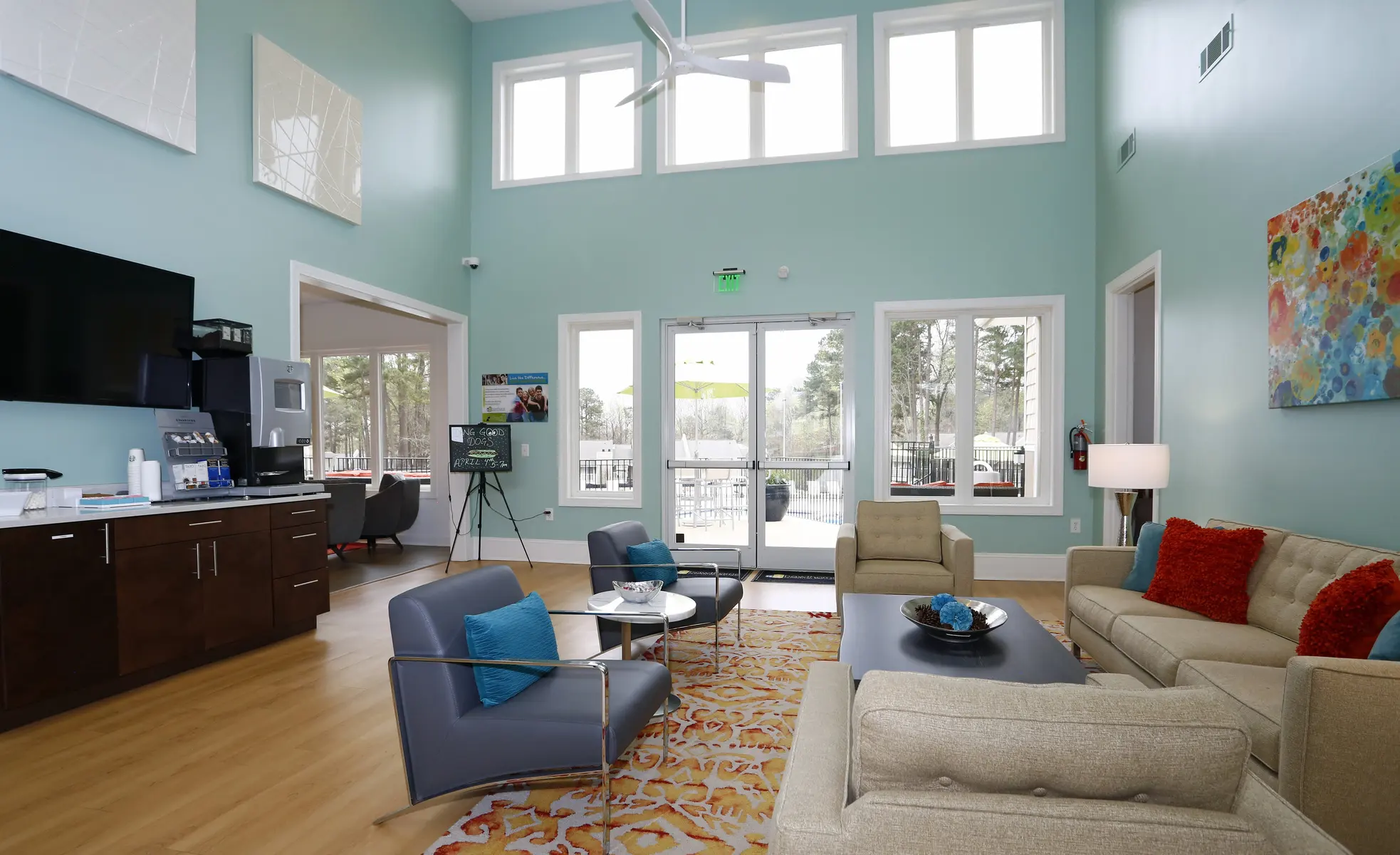 A spacious and modern lounge area with large windows, featuring comfortable seating, a coffee station, and a vibrant rug.