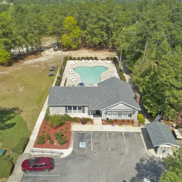 Aerial view of a community center with a pool surrounded by lounge chairs and shaded by trees.