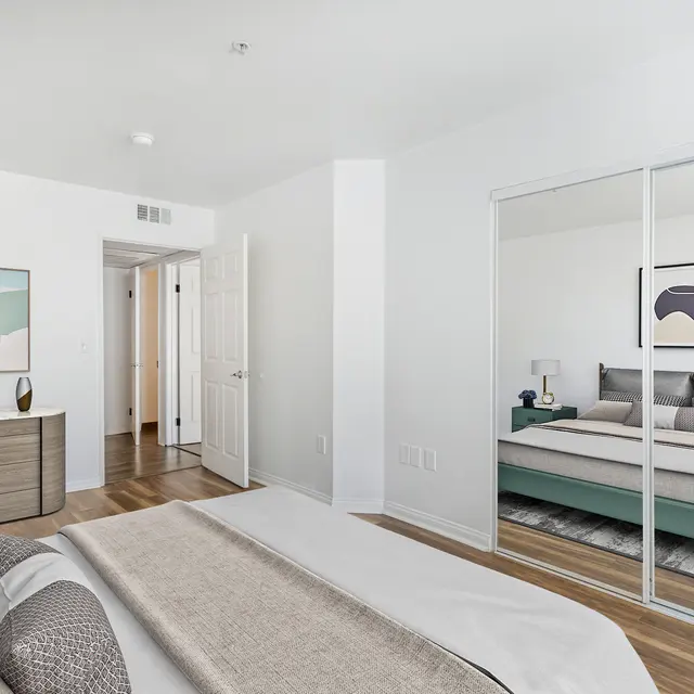 A modern bedroom featuring a bed with grey and white bedding, a mirrored closet, and abstract wall art.