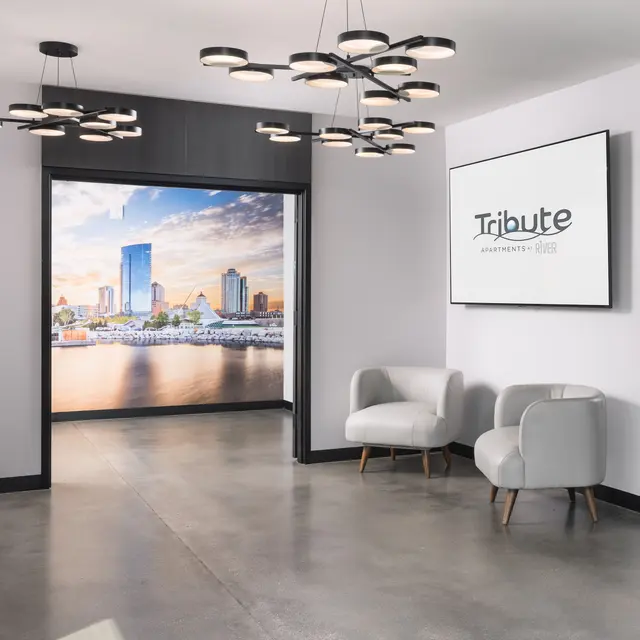 A modern lobby featuring a contemporary chandelier, two light gray chairs, and a large wall mural depicting a city skyline.