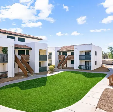 A modern apartment complex with white walls and brown roofs, featuring a green lawn and a clear blue sky.
