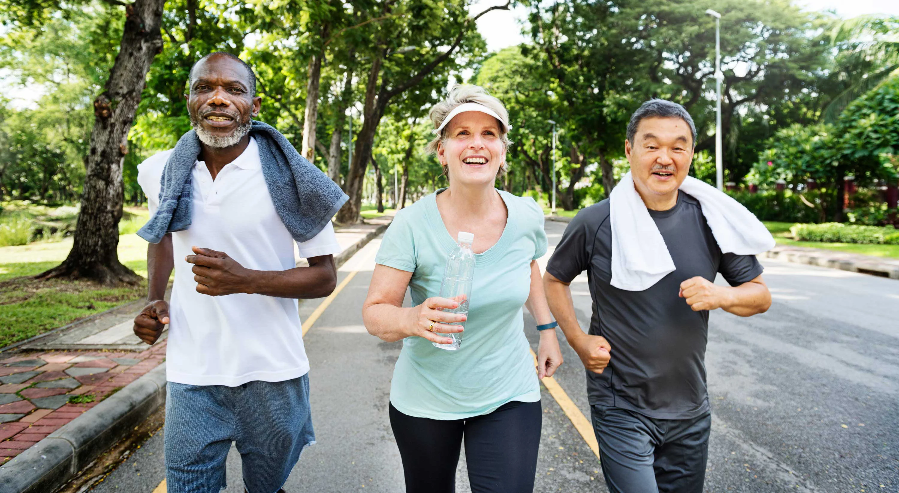Jogging Together in the Park A diverse group of three people jogging together on a sunny day. Two men and one woman, all smiling and enjoying their exercise, with trees lining the path behind them.