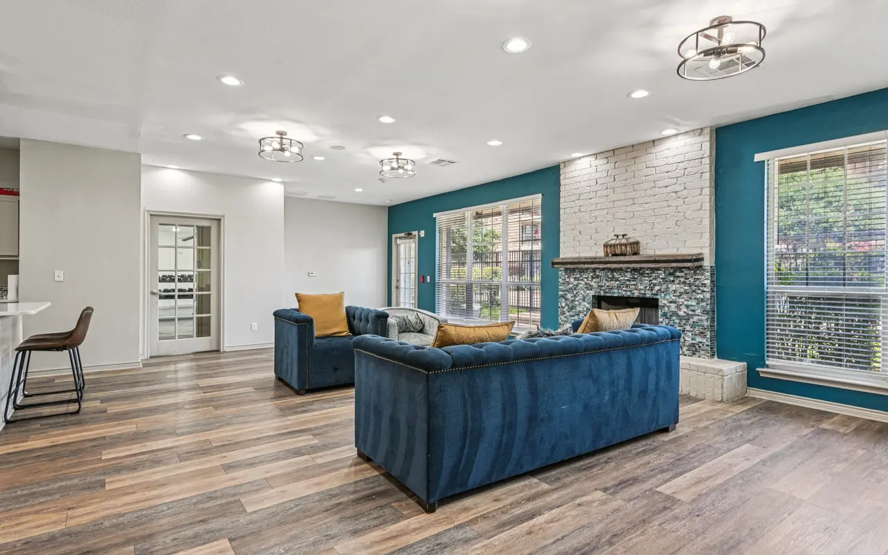A modern living room featuring blue sofas, a stone fireplace, large windows, and wooden flooring.