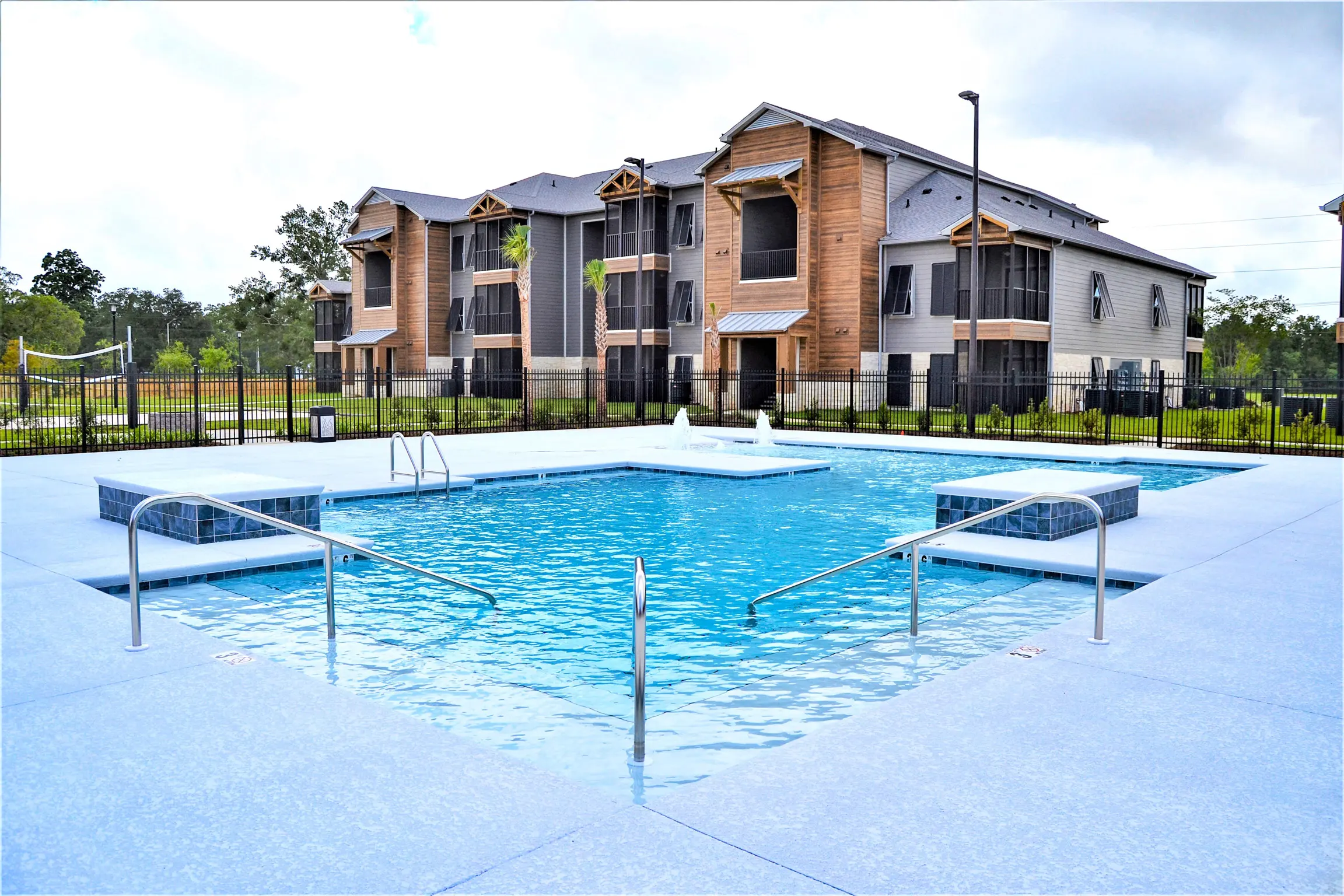 A view of a swimming pool surrounded by a landscaped area and modern apartment buildings in the background.