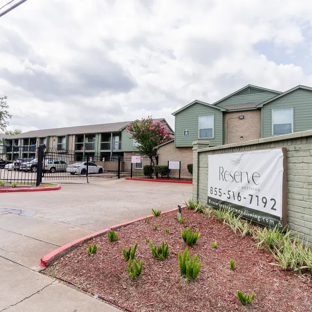 Entrance to the Reserve apartment complex with greenery and parked cars.